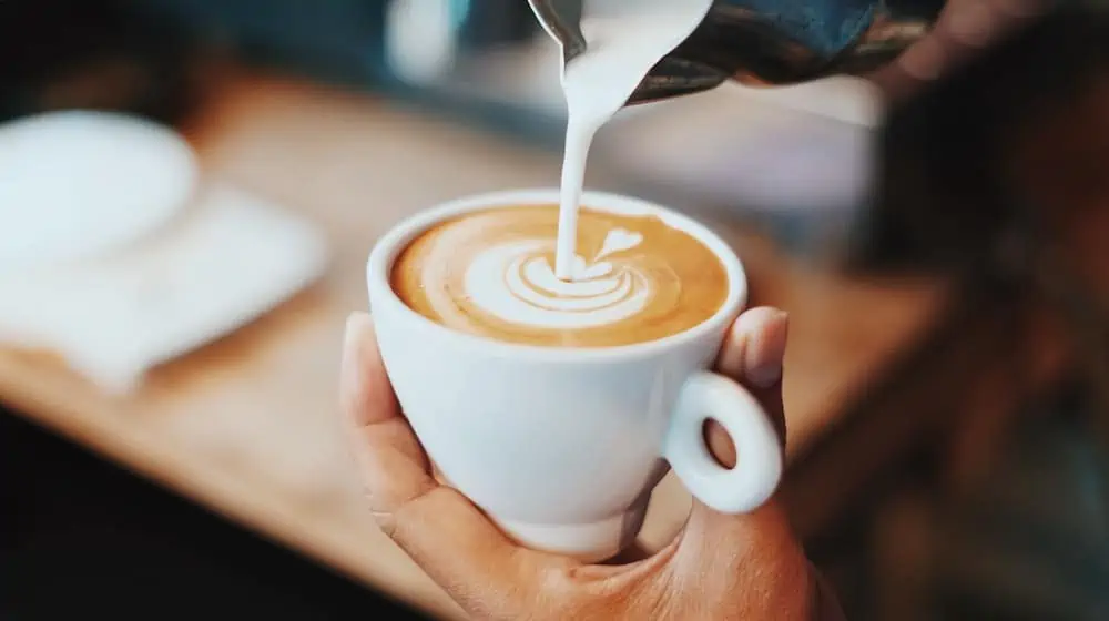 Iemand giet melk in koffie en maakt latte art met een hartje