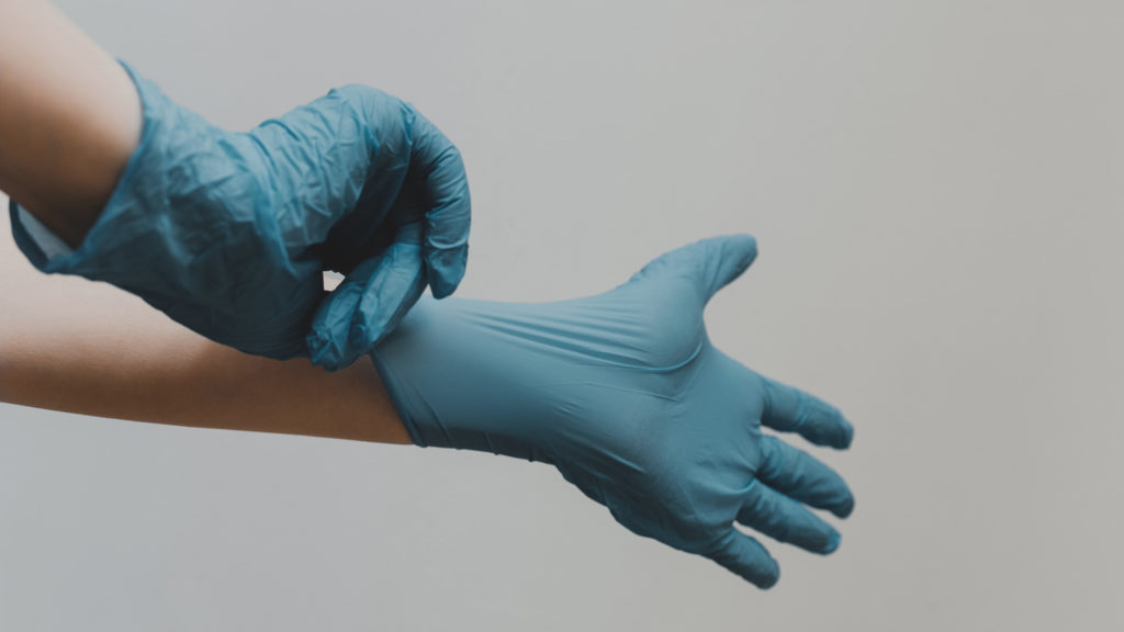 Afbeelding van de handen van iemand die rubberen handschoenen aantrekt.