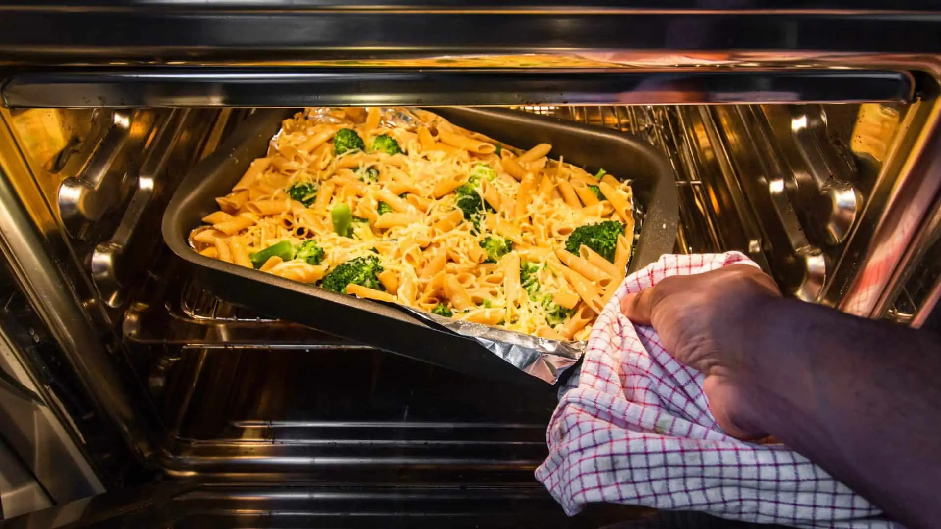 Persoon doet ovenschotel met pasta, kaas en broccoli in de oven.