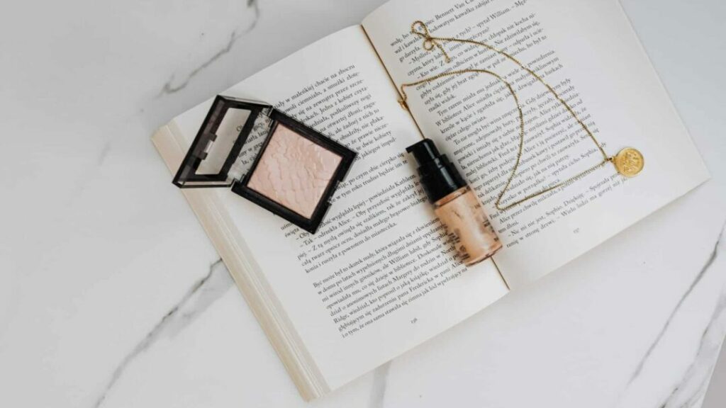 foundation in flacon op een boek met make-updoosje en gouden ketting