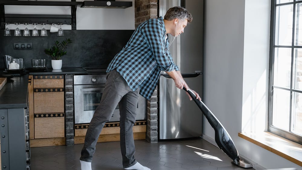 Afbeelding van een man die de keuken stofzuigt. 