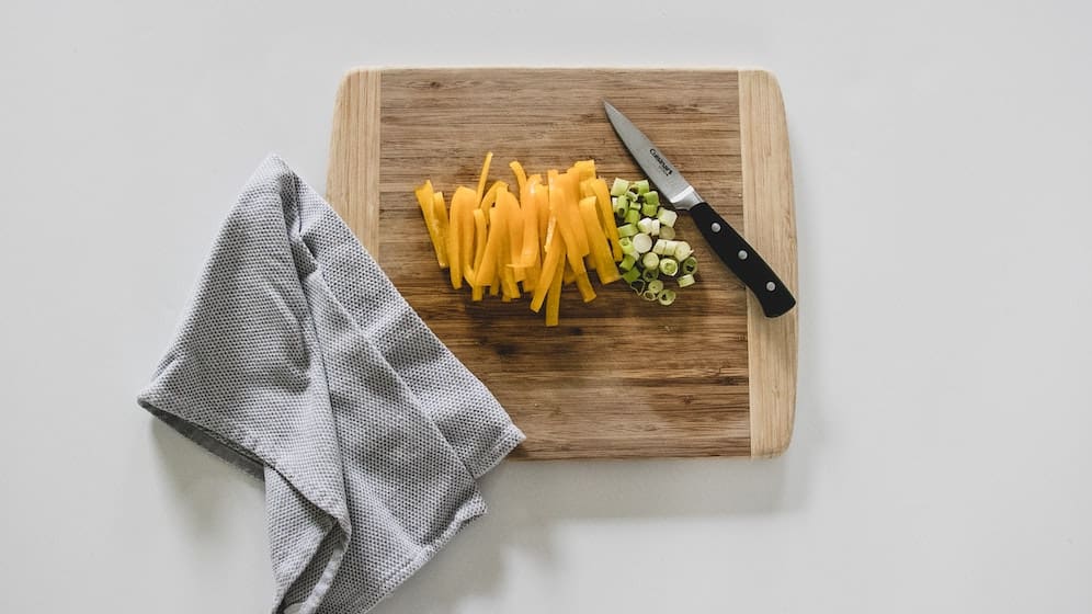 Houten snijplank met een mes, groenten en een doek