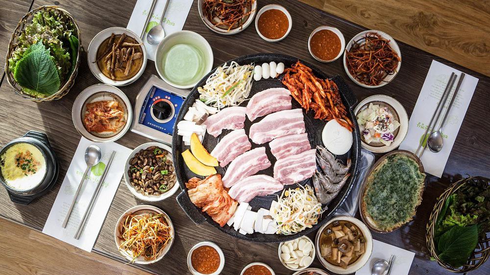 Afbeelding van een gourmetstel met allerlei vleeswaren, vis en groente erop. Om het gourmetstel heen liggen ook etenswaren.