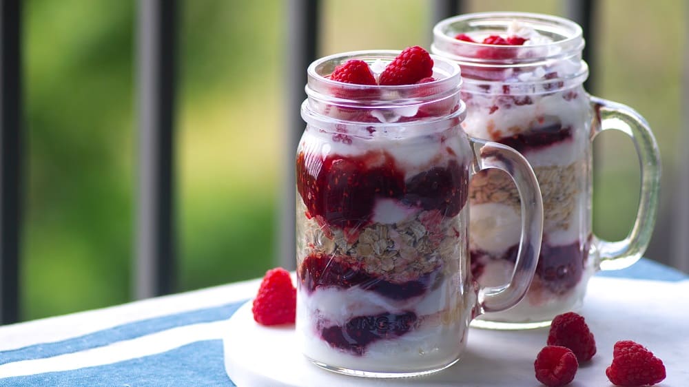 Afbeelding van twee glazen potten met daarin yoghurt, muesli en frambozen. 