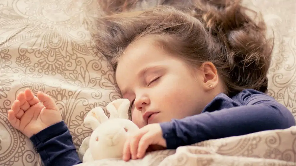 Afbeelding van een kind dat slaapt met een knuffel in haar hand.